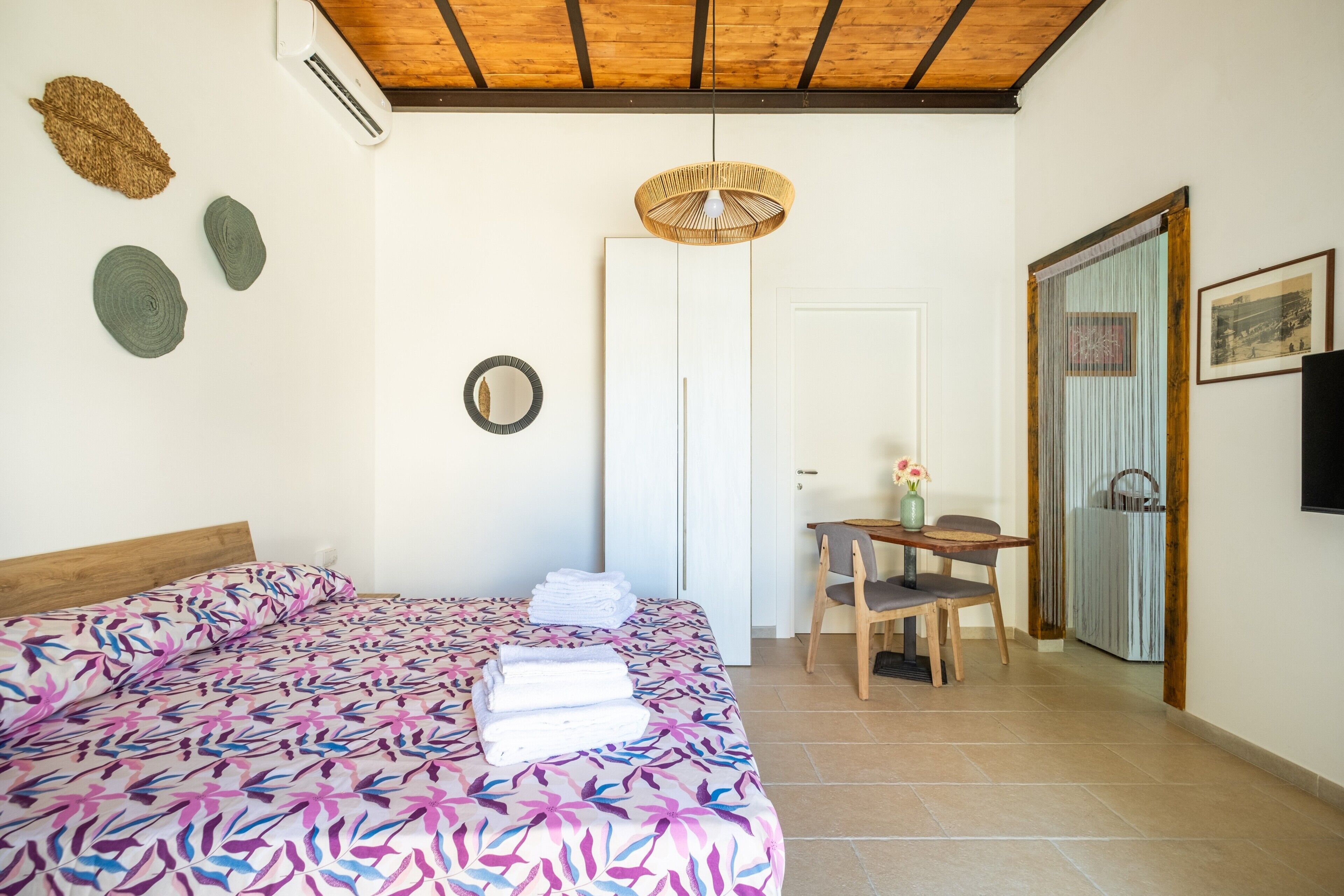 A bedroom with a bed, a desk, a chair, a door, and a wall-mounted TV.