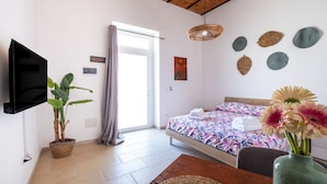 Une chambre à coucher comprenant un lit, un téléviseur, une plante en pot, un vase avec des fleurs et un mur décoré d’assiettes.