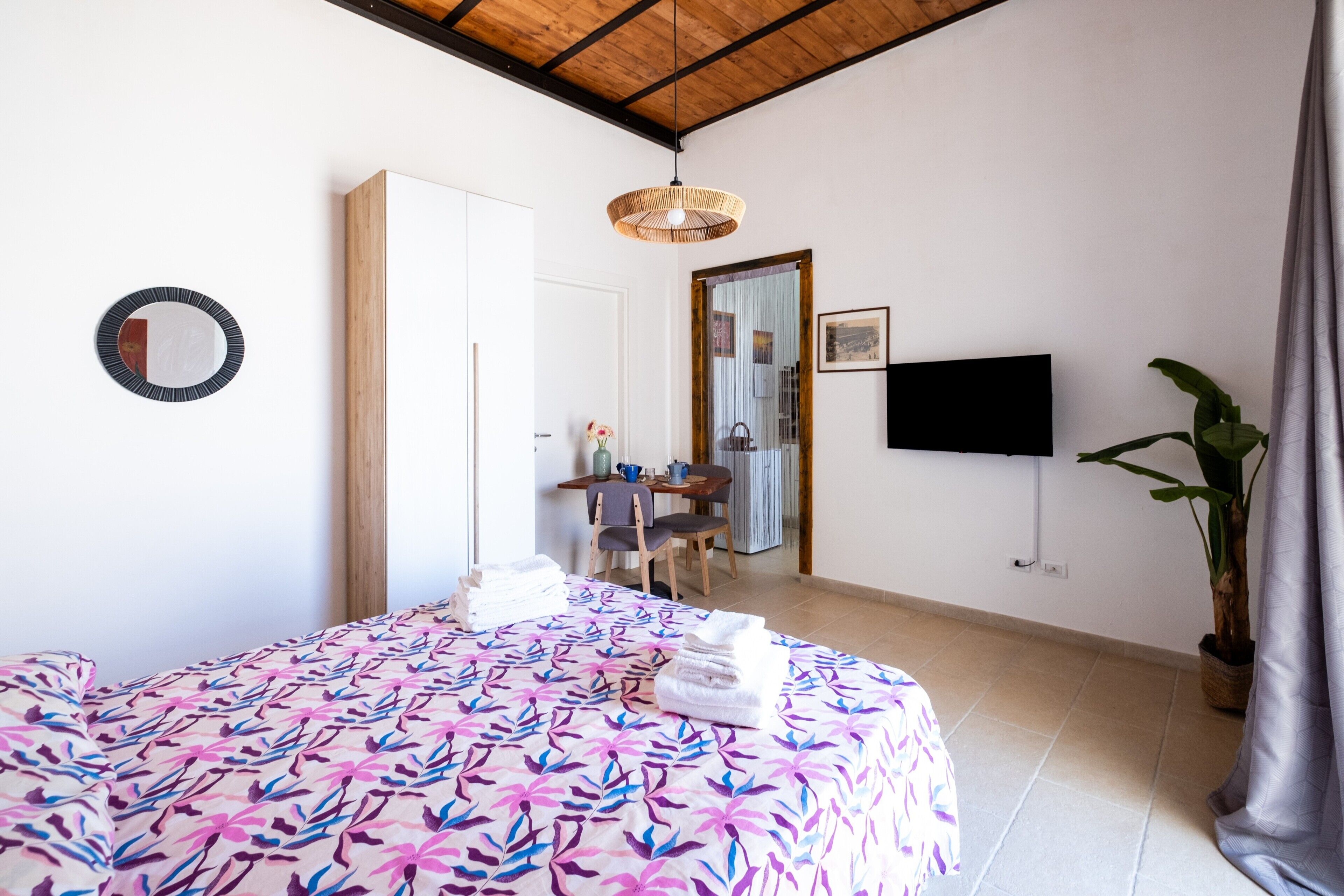Une chambre à coucher comprenant un lit, un bureau, une chaise, un téléviseur et une plante en pot.