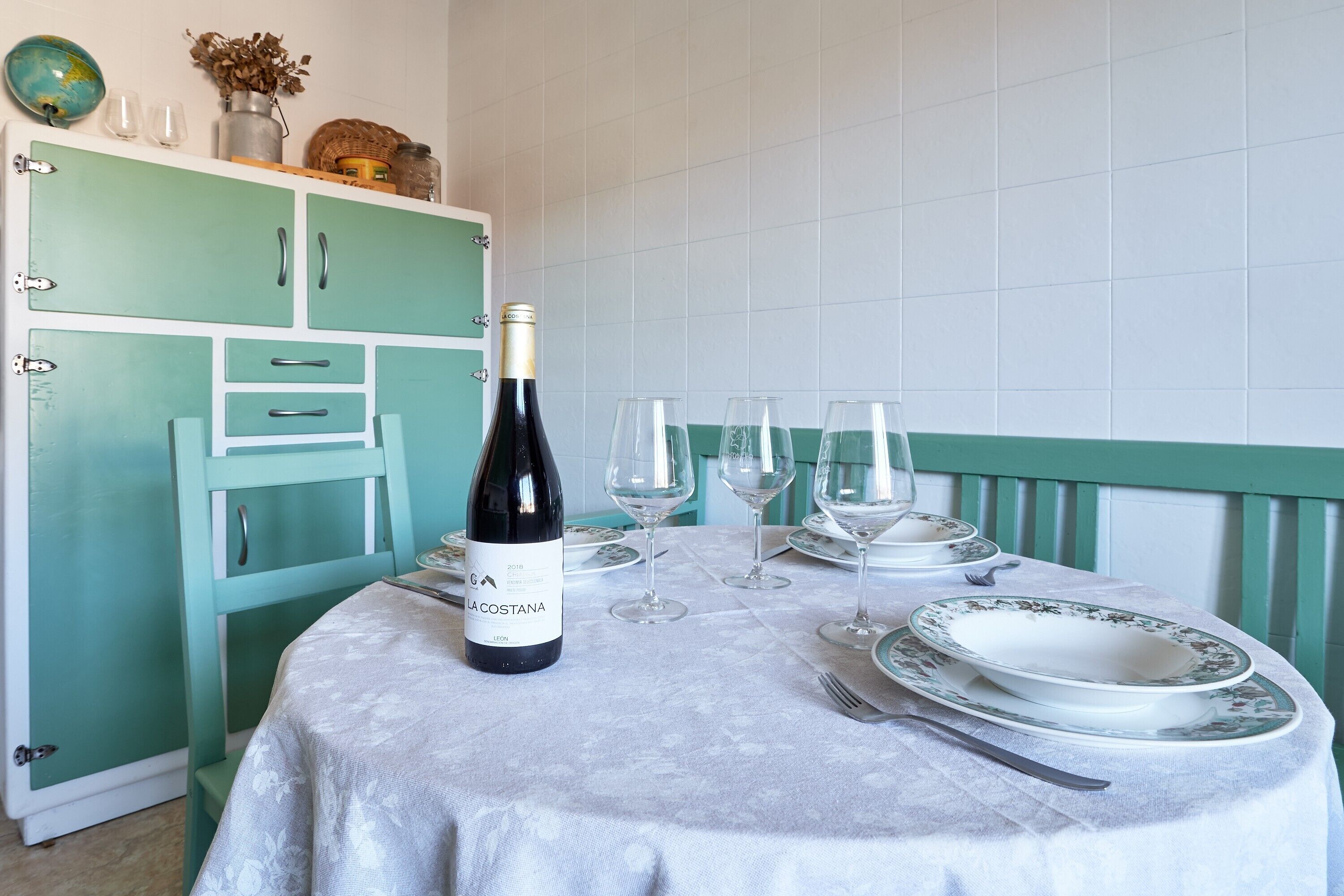 Una mesa de comedor servida con copas de vino, una botella y platos.