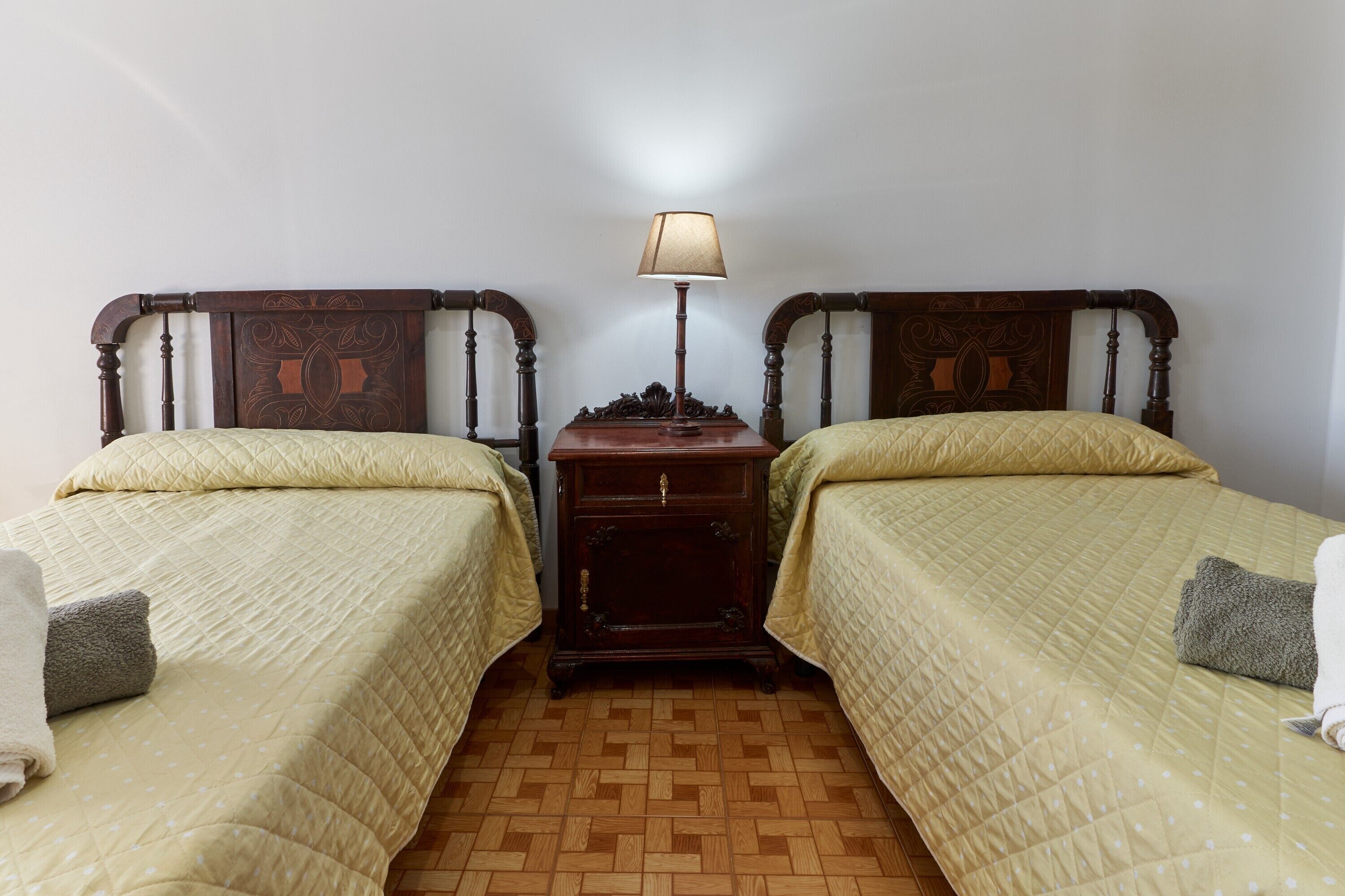 Een kamer met twee bedden, een nachtkastje, een lamp en een houten vloer.