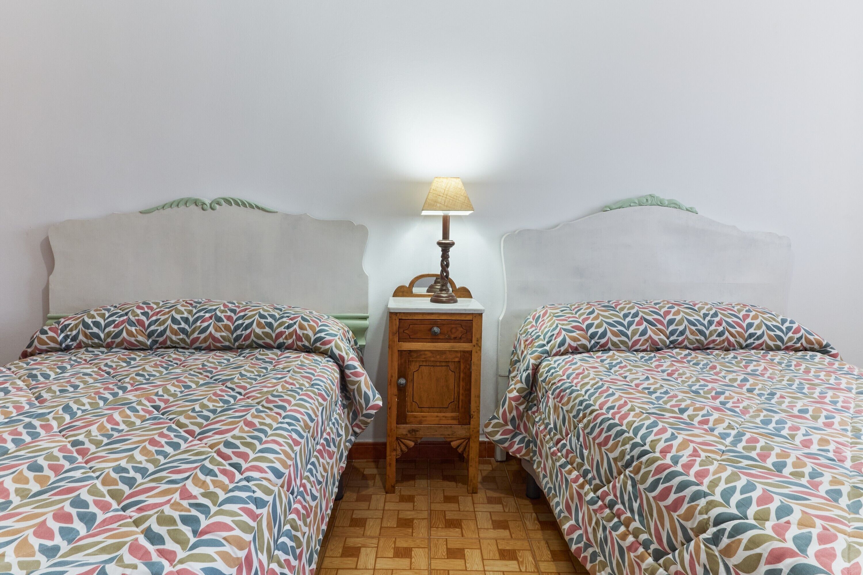 Ein Zimmer mit zwei Betten, einem Nachttisch mit Lampe und einem gemusterten Boden.