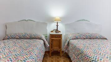 Ein Zimmer mit zwei Betten, einem Nachttisch mit Lampe und einem gemusterten Boden.