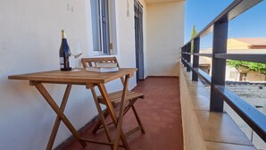Et træbord med en flaske og et glas på en balkon med flisegulv og gelænder.
