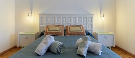 A neatly made bed with a blue quilt, two white nightstands with wall-mounted lamps, and a white headboard with a geometric pattern.