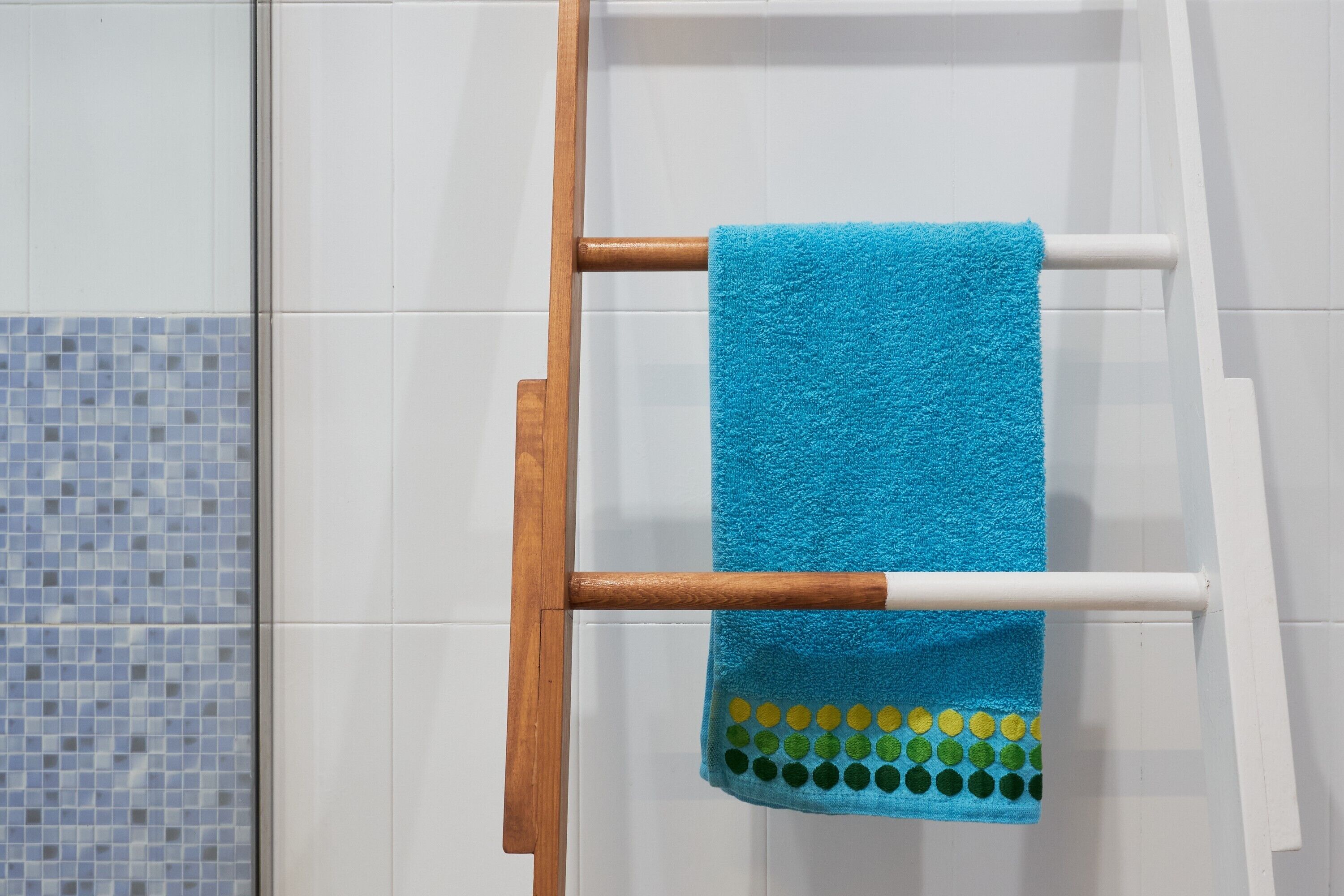 A bathroom with a wooden towel rack holding a blue towel with a green and yellow pattern.