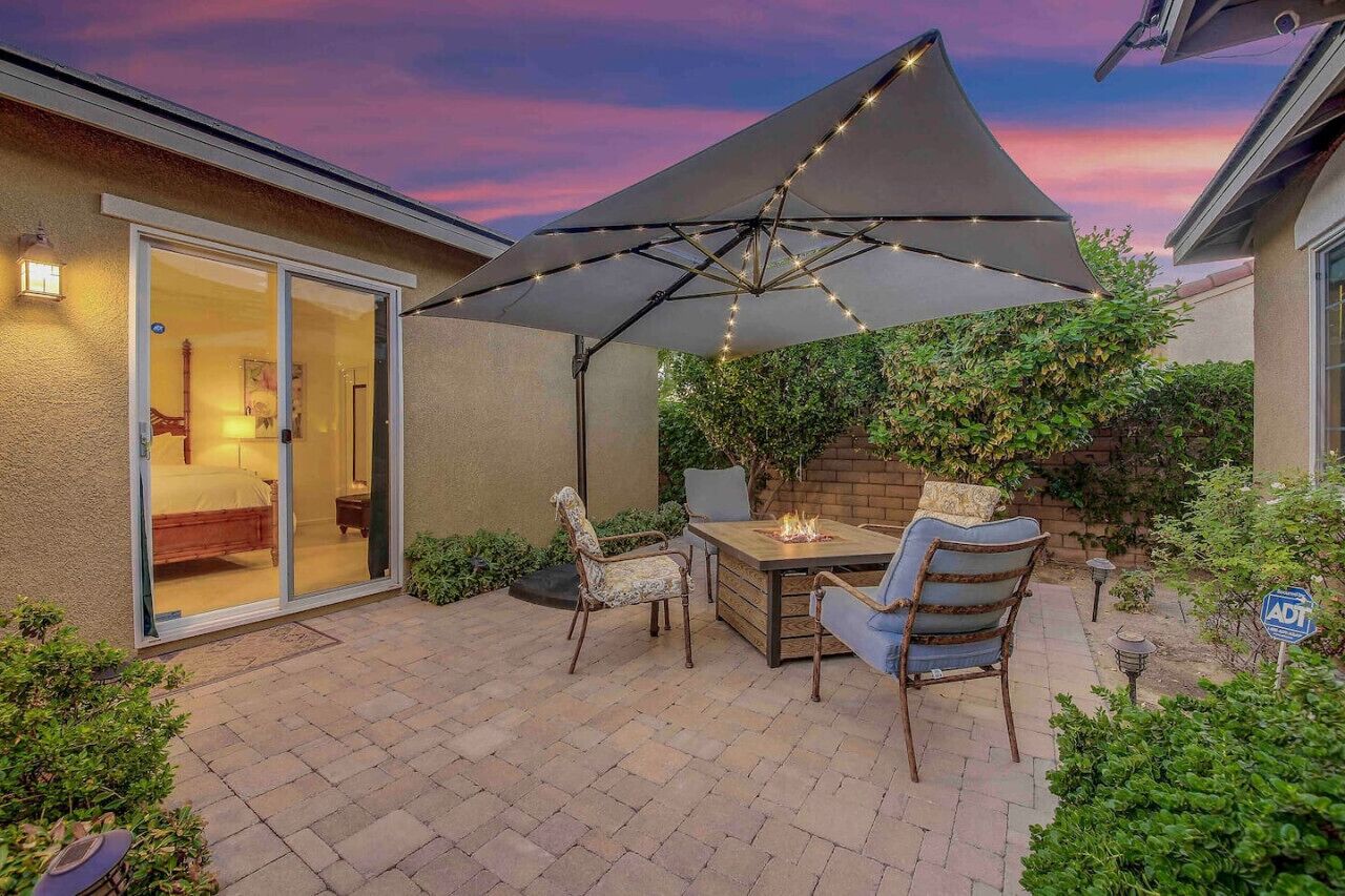An outdoor patio with a table and chairs, a large umbrella, and a fire pit.