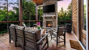 Une terrasse en bois avec des meubles d’extérieur, une cheminée en pierre et un téléviseur à écran plat.