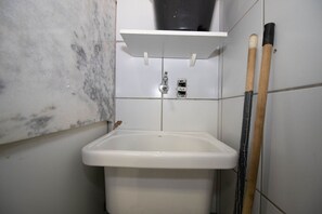Een badkamer met een wit wastafelmeubel, een wit schap erboven en een zwarte pijp aan de muur.
