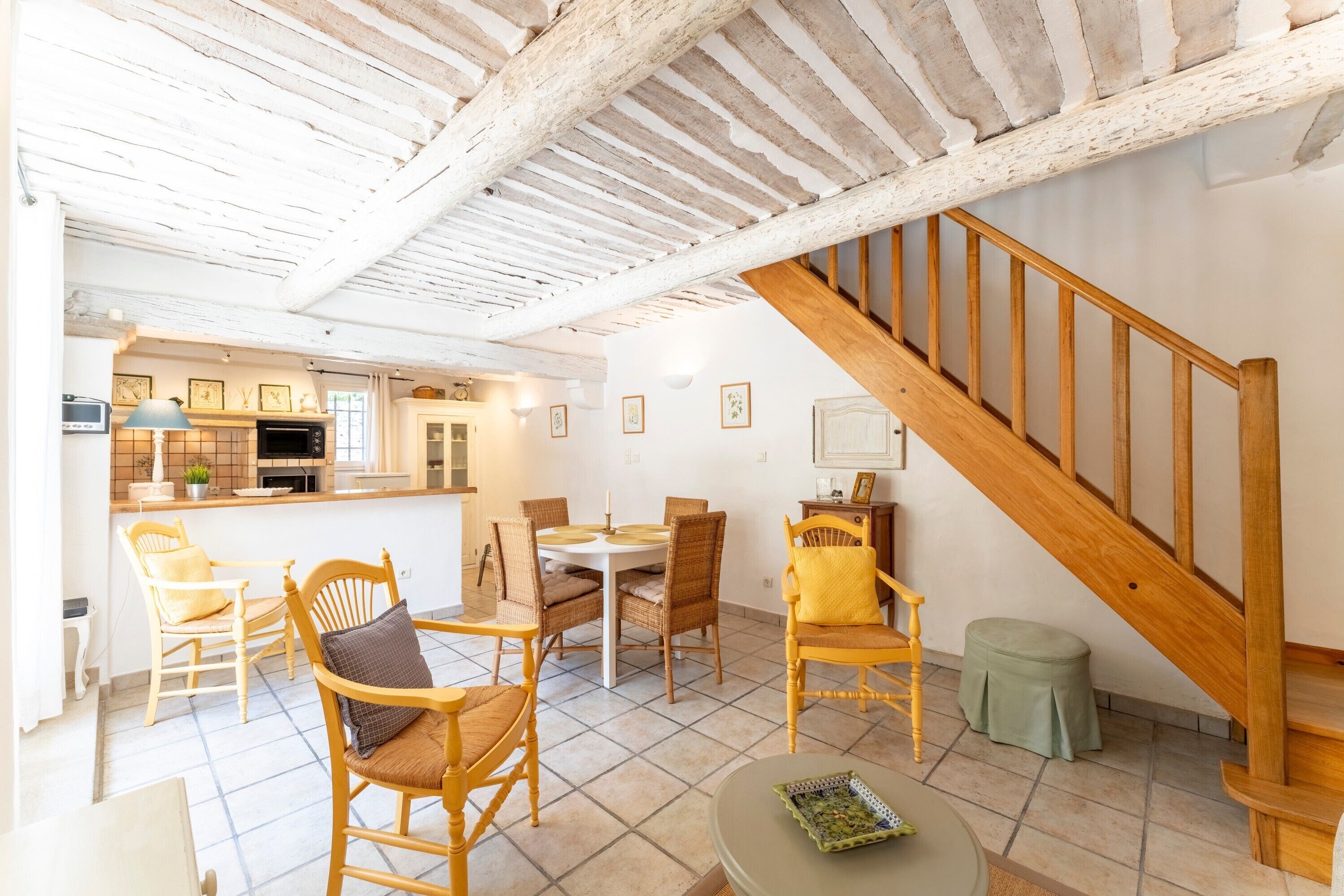 Un amplio espacio habitable con una escalera de madera, una mesa de comedor con sillas y una zona de cocina.