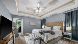 Un dormitorio con una cama grande, un ventilador de techo, un televisor y una ventana con cortinas.
