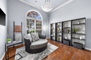 Un salón moderno con un sofá gris, un ventanal grande y una estantería con papel tapiz estampado.