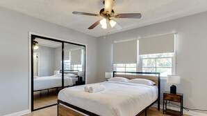 Ein modernes Schlafzimmer mit einem großen Bett, einem Deckenventilator und Blick ins Freie durch ein Fenster.