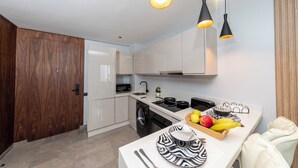 A modern kitchen with a washing machine, a microwave, and a sink. There are hanging lights and a fruit bowl on the counter.