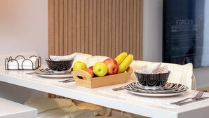 A breakfast setting with a fruit bowl, plates, and cutlery on a white table.