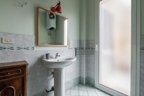 Un bagno con lavandino bianco, mobile contenitore in legno, specchio, lampada rossa e porta doccia in vetro smerigliato.