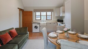 A compact kitchen with a washing machine, a dining area with a round table set for four, and a green sofa with red cushions. - 3 bedroom accommodation in Church Stretton (Church Stretton)