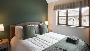A neatly made bed with white and green bedding, a wooden headboard, and a window with a view of buildings outside. - 3 bedroom accommodation in Church Stretton (Church Stretton)