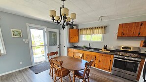 Una cocina con mesa y sillas de madera, estufa y ventana con cortinas.