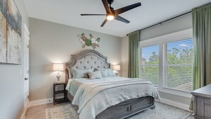 A bedroom with a bed, nightstands, a ceiling fan, a window with curtains, and a view of greenery outside.