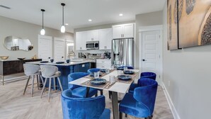 A modern kitchen with white cabinets, stainless steel appliances, and a dining area with blue chairs and a white table.