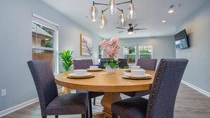 A dining area with a round table, six upholstered chairs, and a ceiling fan.