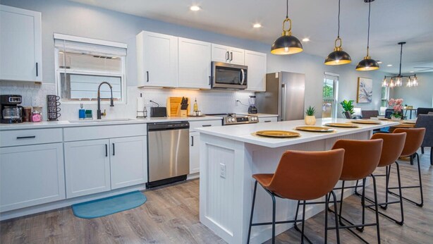 A modern kitchen with white cabinets, stainless steel appliances, and a central island with bar stools.