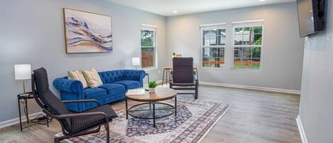 A living room with a blue sofa, a black chair, a round coffee table, and a ceiling fan.