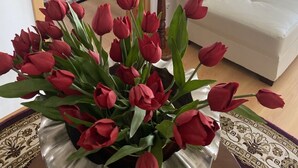 A room with a bed, a white sofa, a painting, and a vase of red tulips.