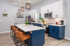 A modern kitchen with white and blue cabinets, a central island with bar stools, and pendant lighting. - Comfort and Style 4BR 3BA Near Riverwalk and Dtown (San Antonio)