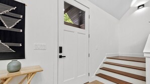 Eine Treppe mit Holzbeschlägen führt zu einer Zwischenebene, dort befindet sich eine weiße Tür mit Fenster und eine Wandleuchte.