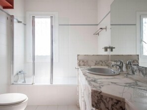 Bathroom features a toilet, glass shower enclosure, and marble sink countertop.