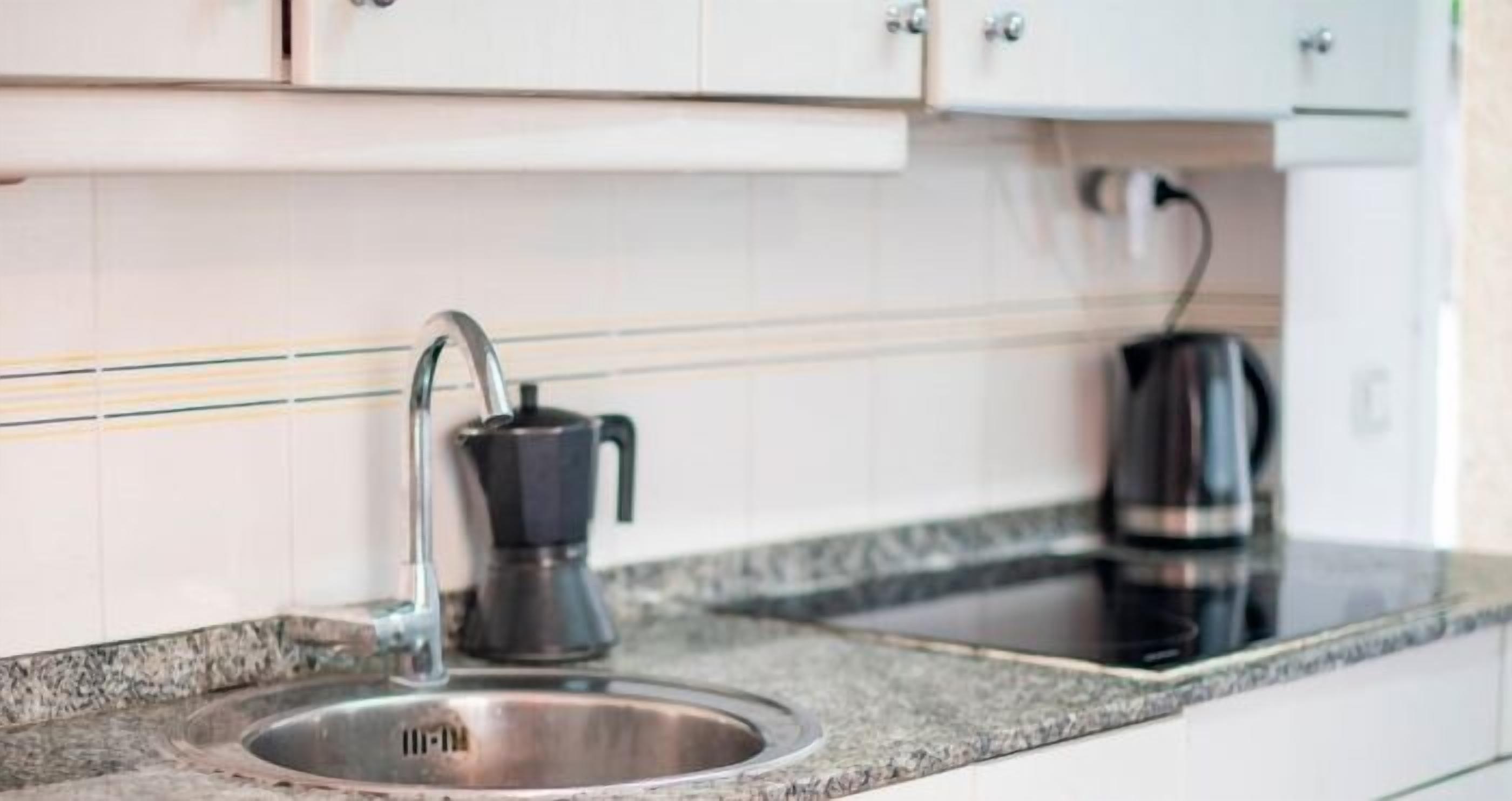 A kitchen with a stainless steel sink, a coffee maker, and a kettle on the countertop.