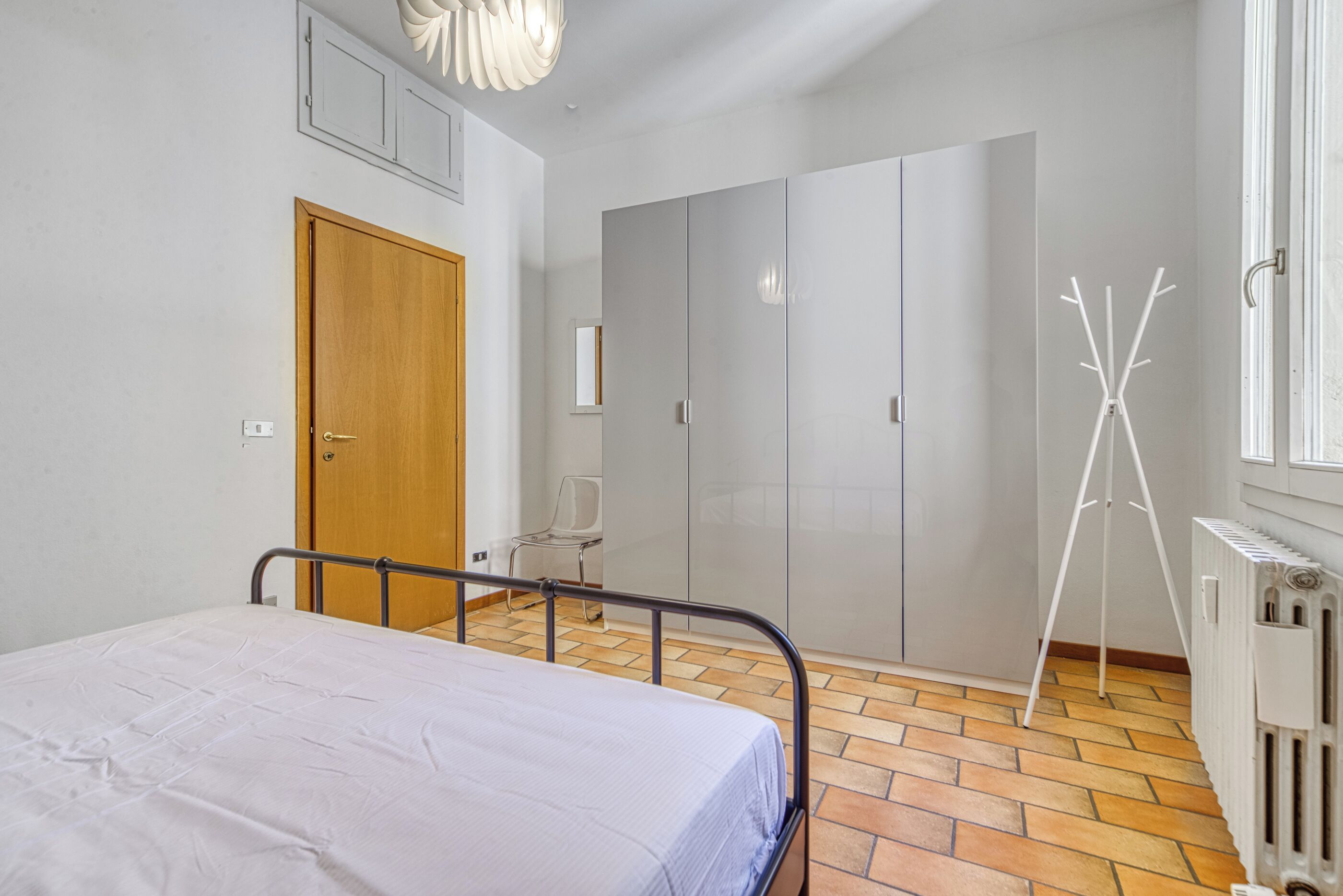 Ein Schlafzimmer mit Bett, Kleiderschrank, Heizkörper und einem Stativ.