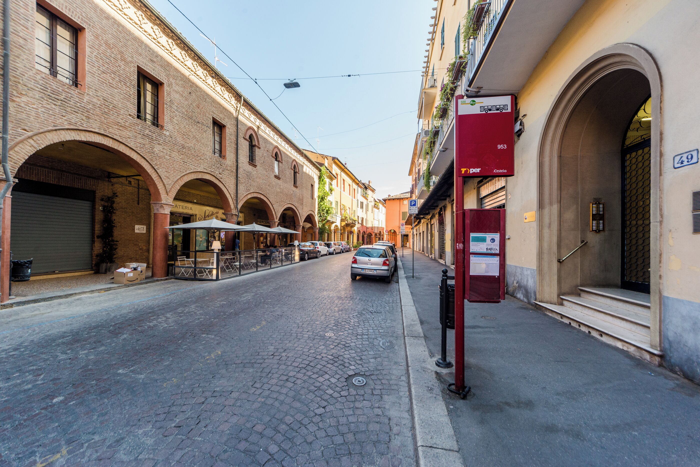 A cobblestone street with buildings on either side, a parked car, and a red mailbox.