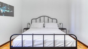 Ein Einzelbett mit Metallgestell, weißer Bettwäsche und zwei Nachttischen.