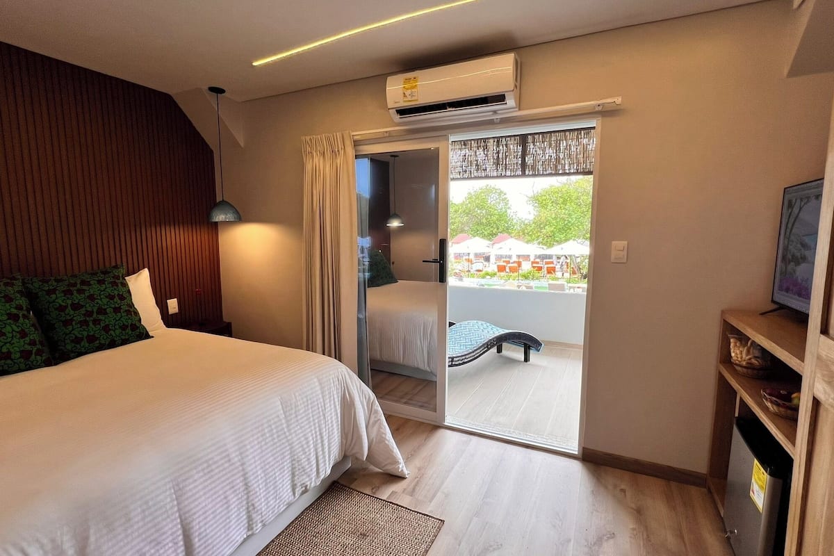A hotel room with a bed, a desk, an air conditioning unit, and a view of the outside.