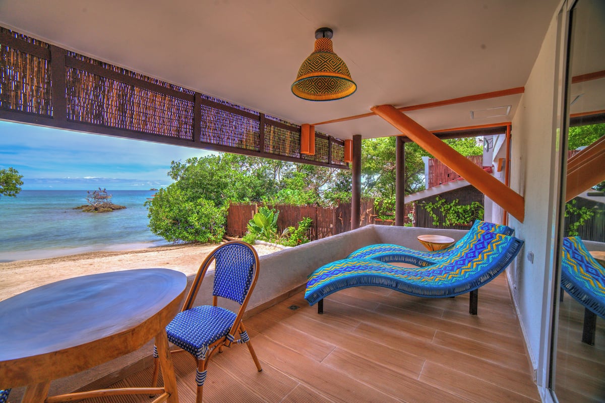 A balcony with a view of the sea, a wicker chair, a cushioned bench, and a table.