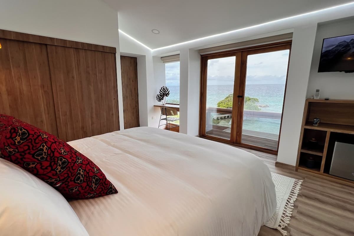 A bedroom with a large bed, a wooden headboard, a TV, and a view of the ocean.