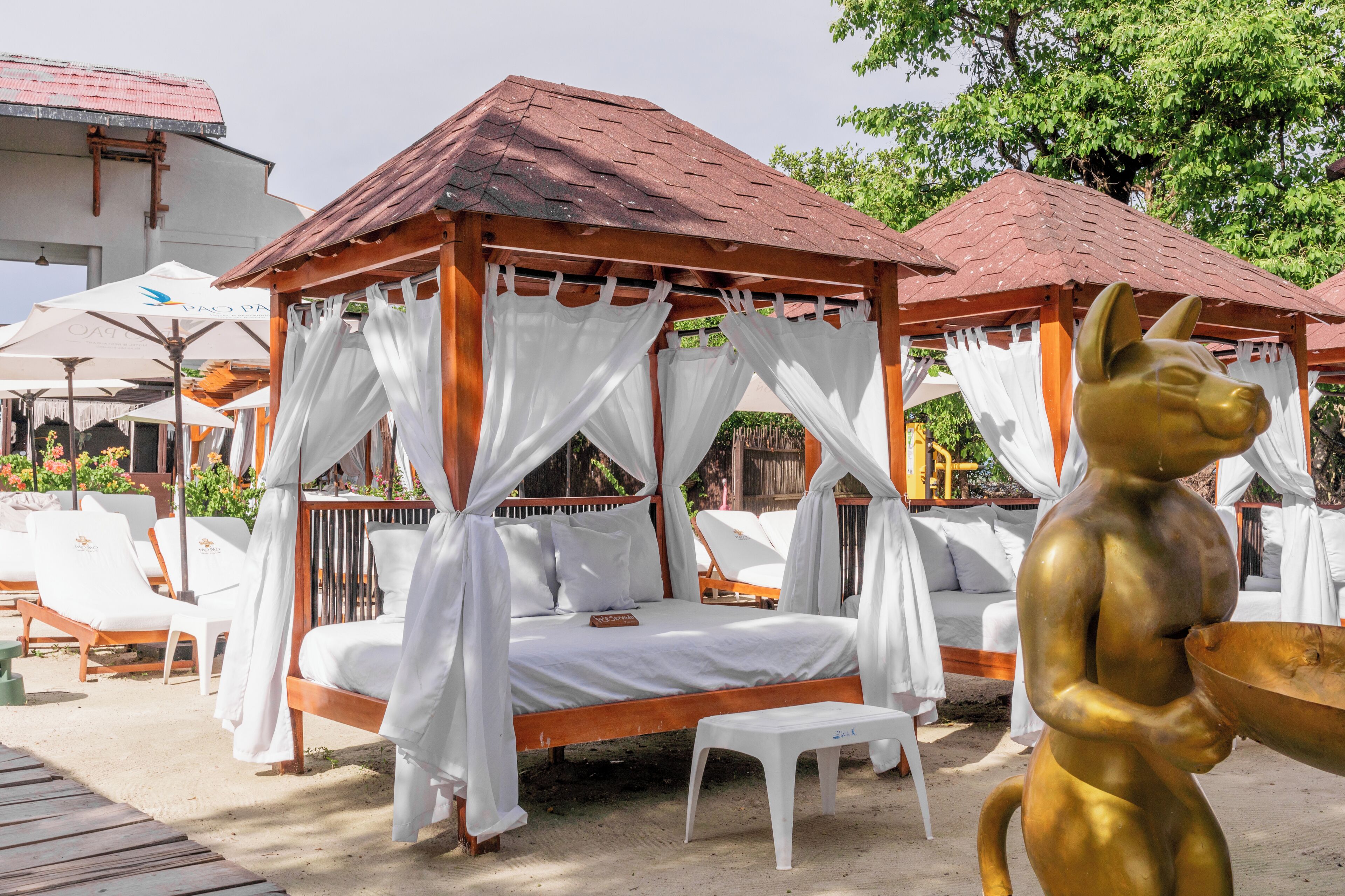 A wooden gazebo with a bed, white curtains, and a golden statue.