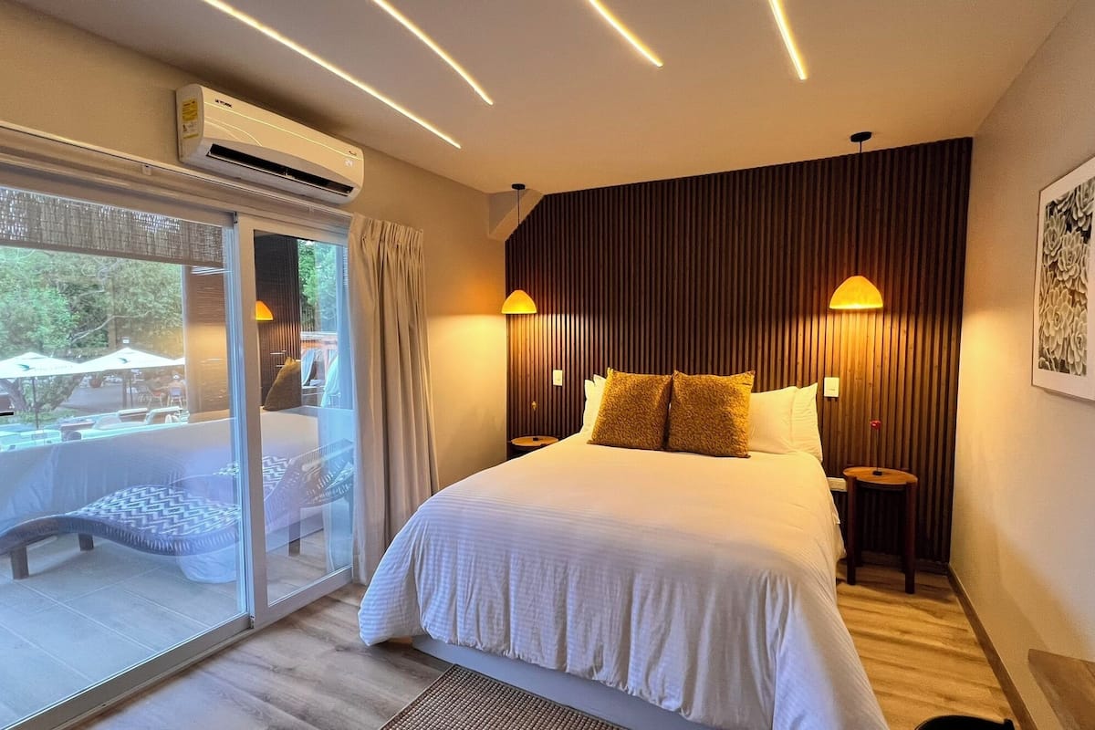 A modern hotel room with a large bed, a sliding glass door to a balcony, and two wall-mounted lamps.