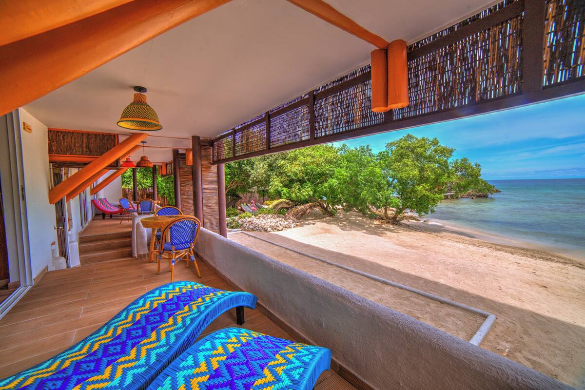 A balcony with a view of a beach and ocean, wooden flooring, and a table with chairs.