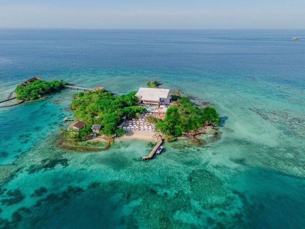 An aerial view of a tropical island with a large building surrounded by lush greenery and clear blue waters.