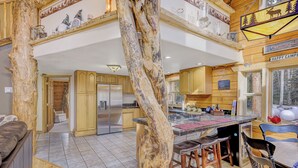 A spacious kitchen with a central island, wooden cabinets, and a large window overlooking a forest.