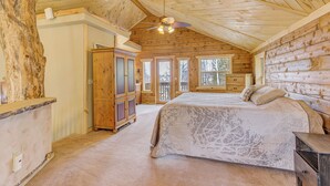 A log cabin bedroom with a large bed, wooden wardrobe, and a ceiling fan.