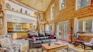 A spacious cabin interior with a large living area, a cozy fireplace, and a kitchen with wooden cabinets.