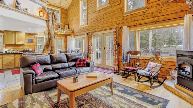 A cozy cabin interior with a leather sofa, rocking chair, and a fireplace.