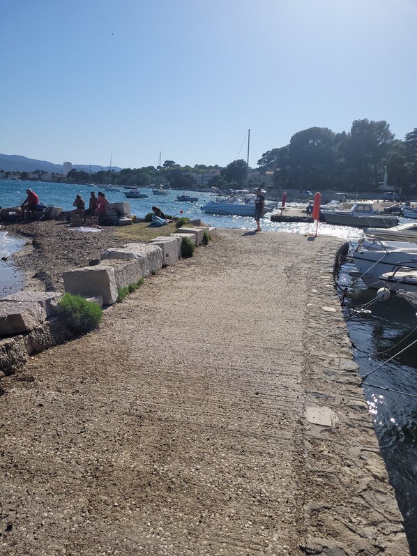 A rocky waterfront with boats docked and people relaxing by the water.