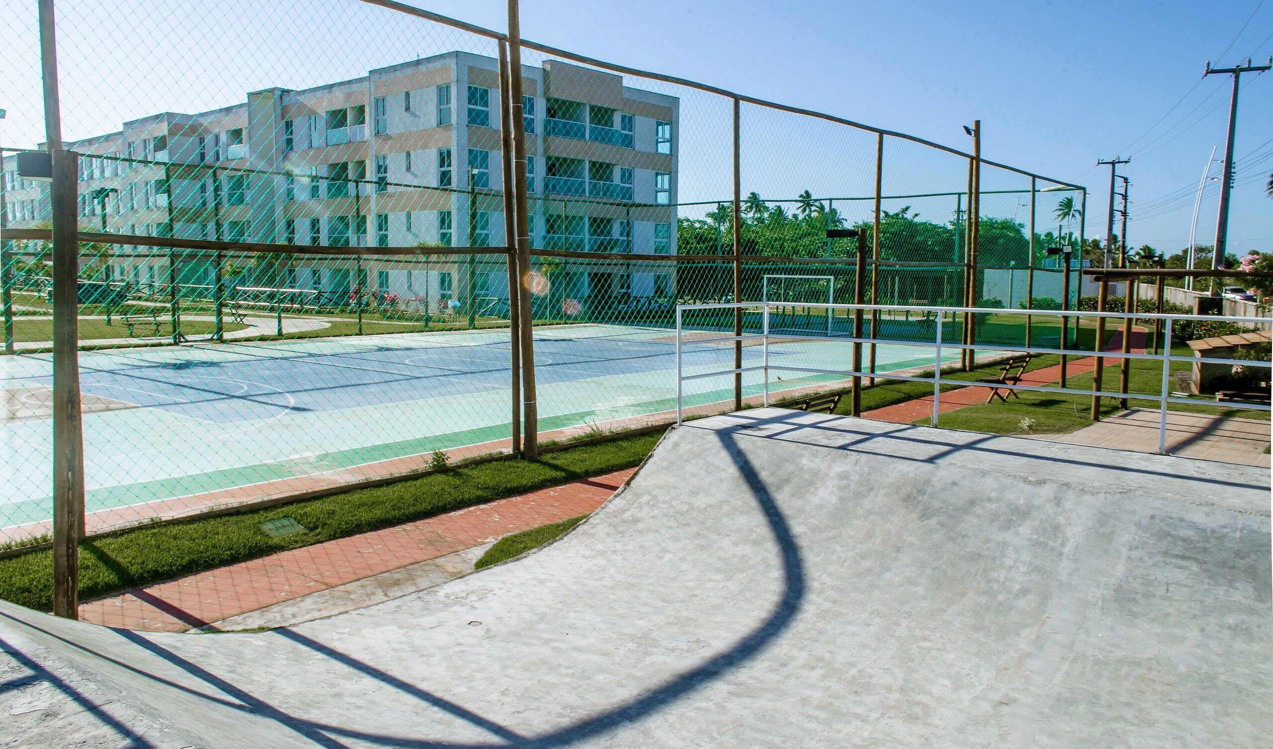 A basketball court with a fence, a concrete ramp, and a building in the background.