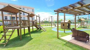 A playground with wooden structures, including slides and climbing frames, and a seating area with wicker chairs.